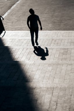 Gözlüklü bir adamın silueti, beton bir merdivenin tepesine çıkıyor, gölgesinden ilginç bir yansıma yaratıyor. Güneş ışığını kontrol et. Sanat, sokak fotoğrafçılığı. Güzel çerçeve bileşimi