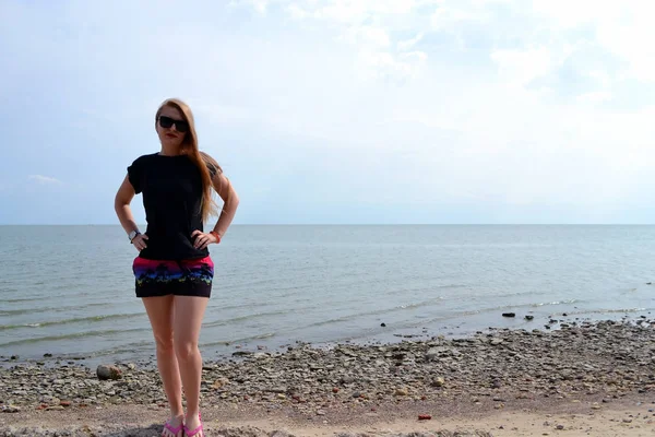 Jeune belle fille élégante dans un simple t-shirt noir posant près de la mer — Photo