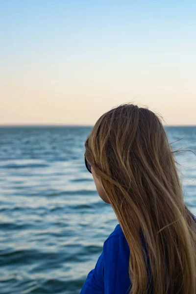 young blonde girl looking sea and blue skies back view