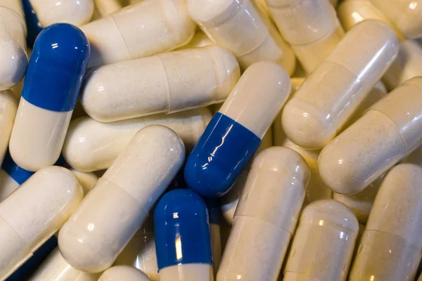 Um punhado de comprimidos brancos e azuis de perto. Cápsulas medicamentos branco e azul . — Fotografia de Stock