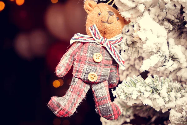 Toy bear in a scarf hanging on the branches of the Christmas