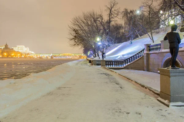 Die Straße in den Schneeverwehungen am Fluss im Park am Abend — Stockfoto