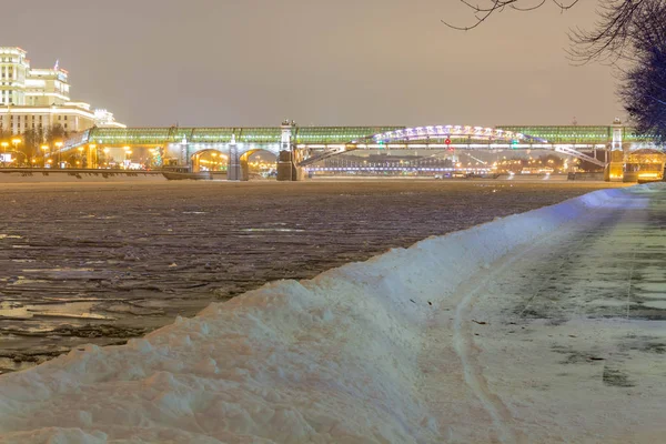 Die Straße in den Schneeverwehungen am Fluss im Park am Abend — Stockfoto