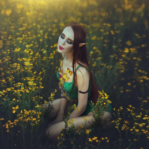 红头发的女孩小精灵穿着绿色的泳装, 坐在一片黄色的花朵上。迷人的年轻女子与黄色蝴蝶在光的光芒. — 图库照片