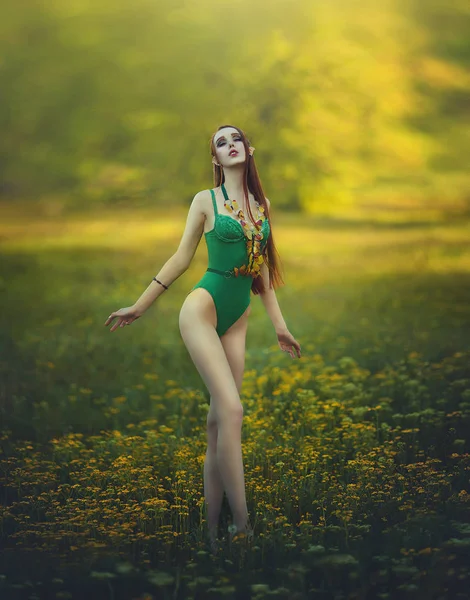 Redheaded long-legged girl elf in a green swimsuit posing in a clearing of yellow flowers. Fantastic young woman with yellow butterflies in the rays of light. — Stock Photo, Image