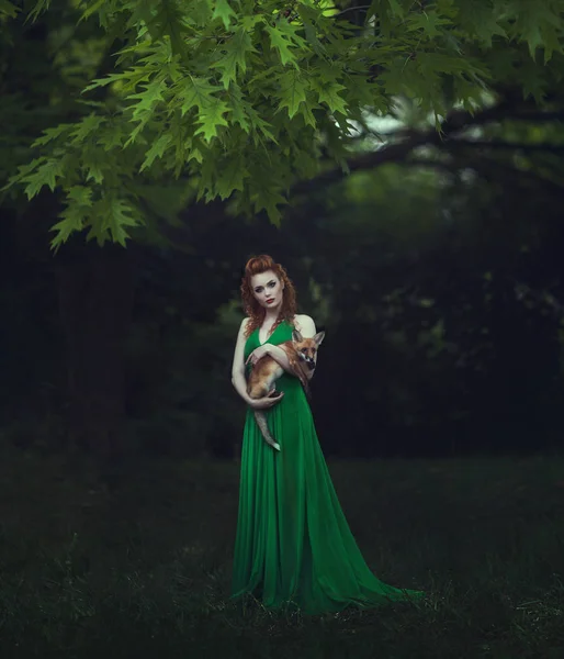 红头发的女孩在一个绿色的礼服与狐狸在童话森林。美丽的年轻女子与年轻的狐狸. — 图库照片