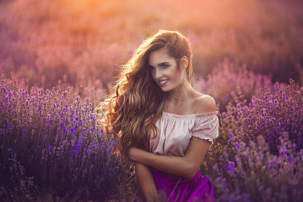 Young woman with charming smile in lavender field at sunset. Portrait of Beautiful happy girl in lavender flowers.