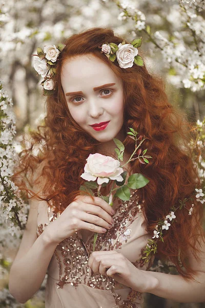 Retrato de una mujer gentil con el pelo largo y rojo con una rosa en un jardín floreciente. Chica pelirroja con la piel pálida y los ojos azules con aspecto inusual brillante . —  Fotos de Stock