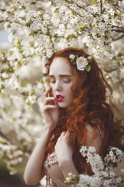 Portrét ženy jemné dlouhé červené vlasy v kvetoucí jarní zahrady. Zrzavý smyslná dívka s bledou pleť a modré oči s jasný neobvyklý vzhled. — Stock fotografie