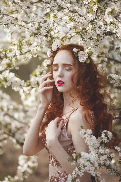 Portréja egy kedves nő hosszú vörös haja az egy virágzó tavaszi kert. Vörös hajú érzéki lán sápadt bőr, és a kék szeme, világos szokatlan megjelenése. — Stock Fotó