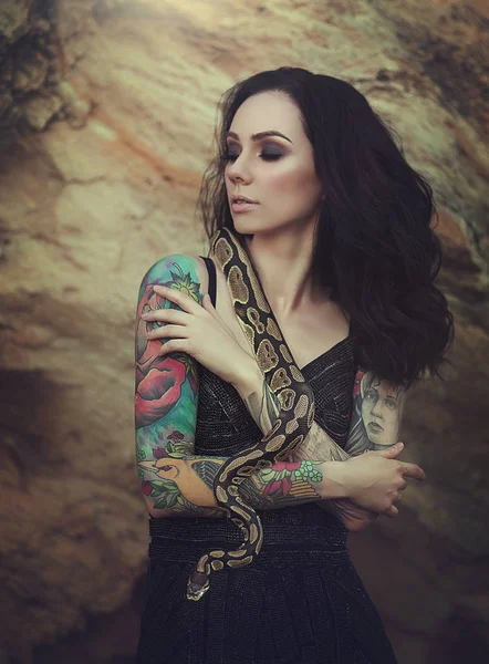 Портрет брюнетка жінка з татуюваннями позують з змія. Дівчина в пустелі з Python. — стокове фото