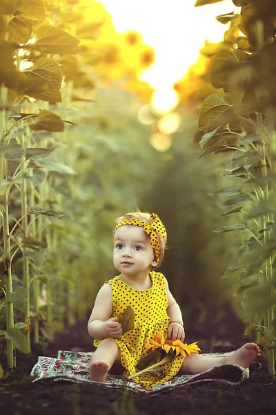 Glückliches kleines Mädchen auf dem Feld der Sonnenblumen im Sommer. ein kleines Mädchen in einem gelben Kleid sitzt in einem Feld von Sonnenblumen. — Stockfoto