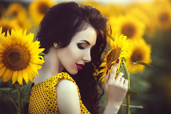 Portret van sensuele mooie brunette vrouw met gesloten ogen in gele jurk in zonnebloemen veld bij zonsondergang. — Stockfoto