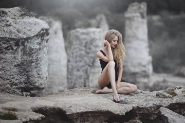 Yıkılmış bir kayaya oturan güzel sarışın... Yaz plaj kavramı. Seksi yaz kadın vücut.