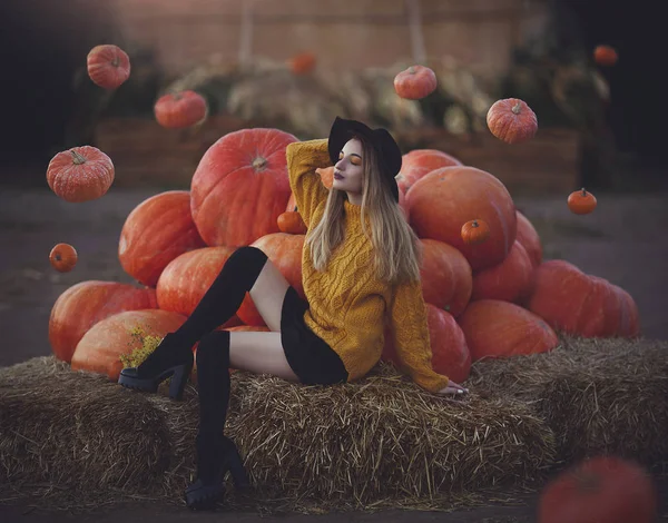 Moderne jonge heks oproept levitating pompoenen. Mooi meisje in een hoed in de buurt van grote pompoenen. — Stockfoto