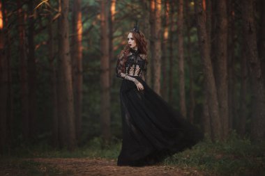 Soluk cilt ve siyah bir taç çok uzun kızıl saçlı ve bir puslu peri ormandaki bir siyah uzun elbise ile güzel bir Gotik prenses. Karanlık Kraliçe kostümü. Sanatsal işleme.