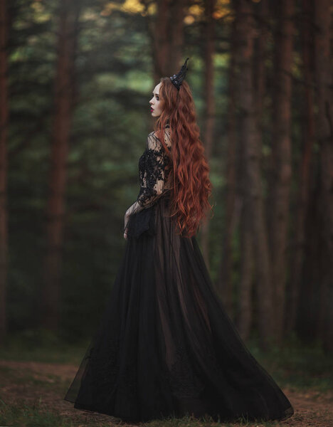 A beautiful gothic princess with pale skin and very long red hair in a black crown and a black long dress walks in a misty fairy-tale autumn forest. The costume of the dark queen. Back view. Artistic processing.
