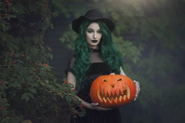 Yeşil ile Halloween cadı oyulmuş bir korkutucu Kabak tutuyor. Siyah şapka ve kabak kostüm güzel genç kadın. Halloween Tema.