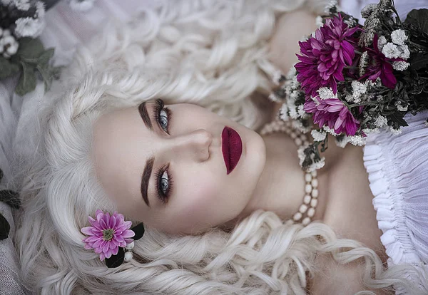 Retrato de uma princesa incrivelmente bonita com cabelo branco. Uma jovem mulher com olhos azuis está de plantão em flores . — Fotografia de Stock