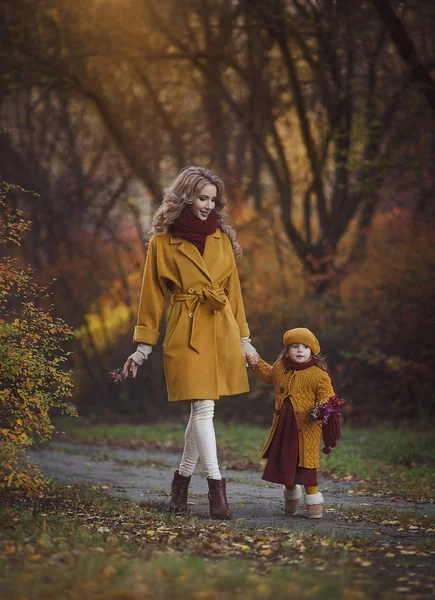 Gelukkig moeder en dochter in kleren van herfst bloemen lopen in het najaar Park. — Stockfoto