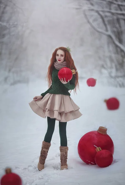 Piękna Rudowłosa dziewczyna jak lalka z Christmas ogromne czerwone kulki spacery w lesie bajki zimowe. Kartki świąteczne. — Zdjęcie stockowe
