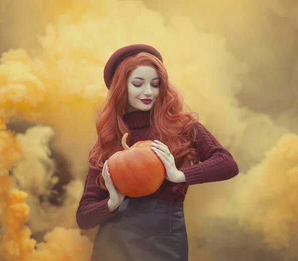 Een roodharig meisje met een pompoen in gele rook. vrouw op een gele herfst achtergrond. — Stockfoto