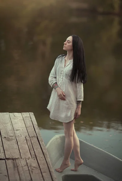 A young woman stands on a boat near the water. Nymph girl at the lake.