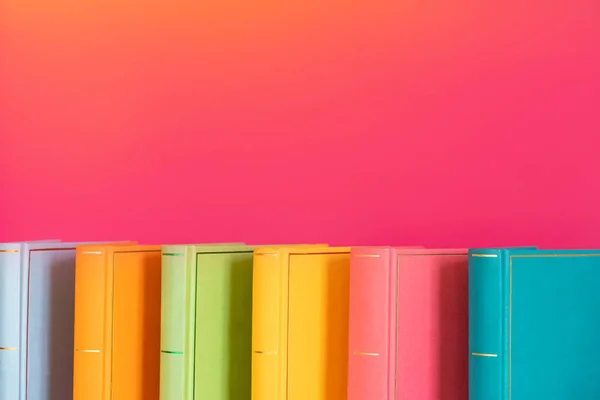 Simple composition of hardback multicolored books, raw of books on pink background. Books stacking with no labels, blank spine Back to school Copy Space Education background Office supplies .