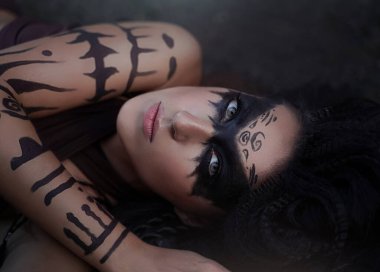 Vahşi bir Amazon kızının yakından çekilmiş portresi. Uzun siyah saçlı ve ritüel makyajlı şaman kız..