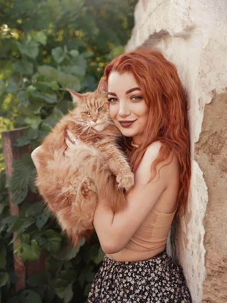 Ragazza dai capelli rossi con un gatto rosso in campagna. Foto Stock Royalty Free