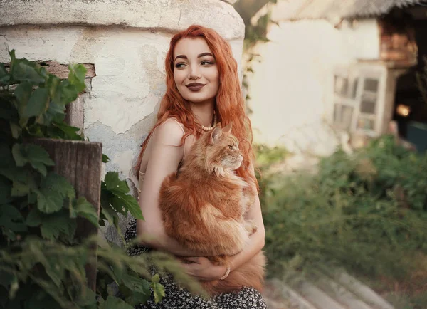 Ragazza dai capelli rossi con un gatto rosso in campagna. Foto Stock