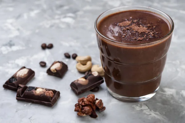 Chocolate smoothie on a glass with coffee beans and nuts on grey stone  background