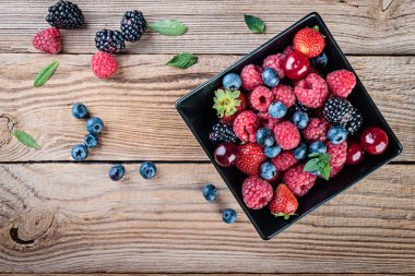 Ahududu, böğürtlen ve yaban mersini rustik ahşap arka plan üzerinde siyah bir tabak içinde görünüm top.