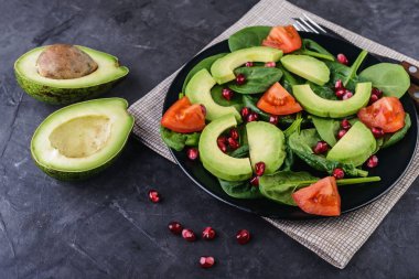 Sağlıklı salata avokado, domates, nar ve bebek ıspanak siyah bir zemin üzerine 