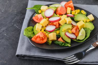 Domates, ıspanak, peynir, turp ve Mısır sağlıklı gıda kavramı koyu arka plan üzerinde siyah bir plaka ile taze avokado salatası.