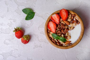 Sağlıklı kahvaltı müsli, çilek ve gri arka plan üzerinde kase fındık ile. Sağlıklı gıda kavramı. Düz yatıyordu.