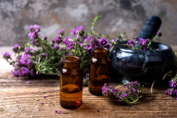 thyme essential oil on a  bottle, mortar and fresh thyme bunch  on a wooden table