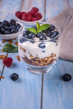 mavi ahşap arka plan üzerinde bir bardak yoğurt ve taze çilek ile granola 