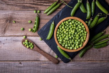 Ahşap arka planda kabuklu taze yeşil bezelyeler.