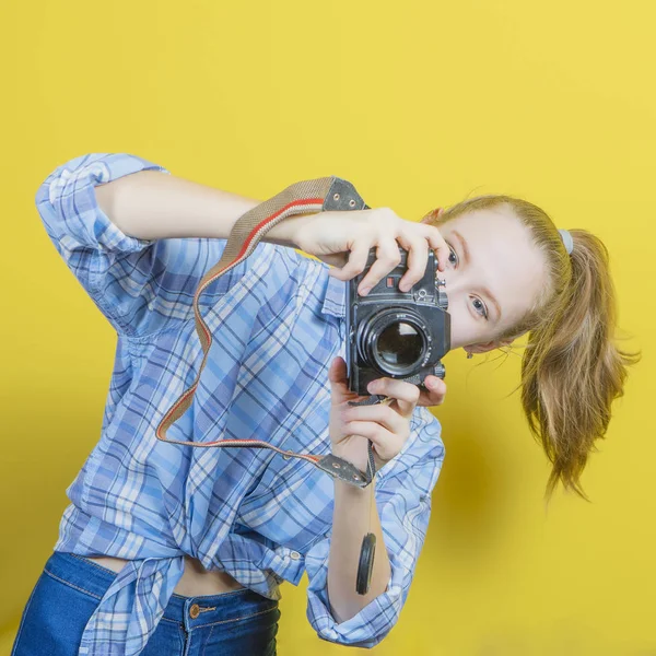 Portret van een verrassingsmeisje met een camera in de hand op een gele achtergrond. Geïsoleerde studio. — Stockfoto