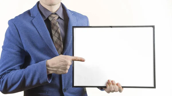 Hombre de negocios con traje sostiene una hoja de papel en blanco, y le señala con el dedo, sobre un fondo blanco —  Fotos de Stock
