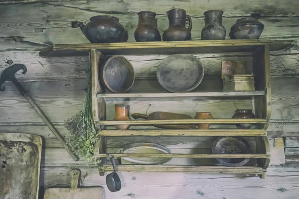 Antique dishes on a wooden shelf. Old scales and an ancient iron with an earthenware jug and glass bottles against a wooden wall on which dried herbs.