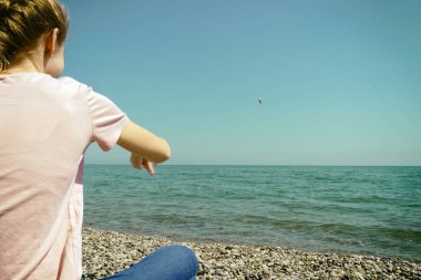 arkasından genç kız sakin bir denize çakıl taşları atar