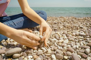 Bir çakıl taşının üzerinde oturan genç. El mavi deniz kıyısında taş döşeme bir taş koymak.