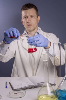 Laboratuvar çalışmaları, mavi lastik eldivenli bir adam test tüpü döktü, bir test tüpünden analiz alır.