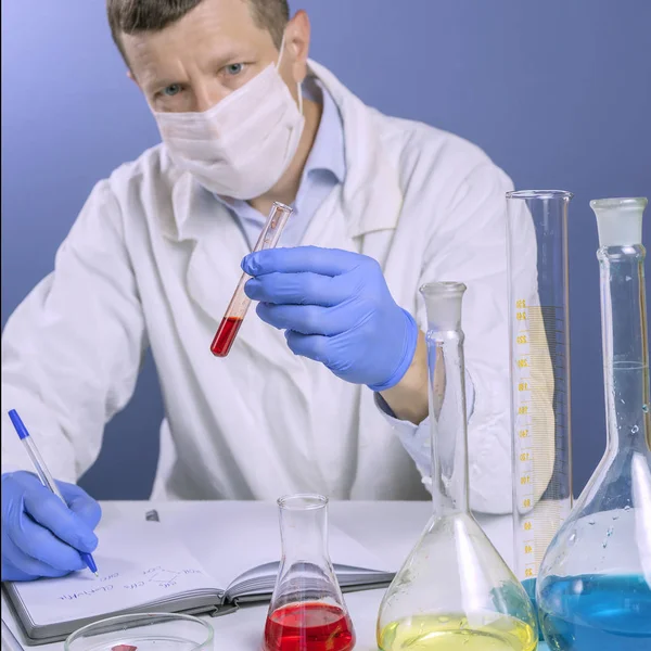 Вчений у білій формі та масці записує свої наукові записки після перегляду тестів у лабораторії . — стокове фото
