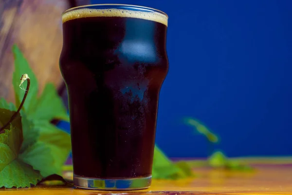 Verre de stout sur une table en bois avec des feuilles de houblon sur fond de tonneaux — Photo