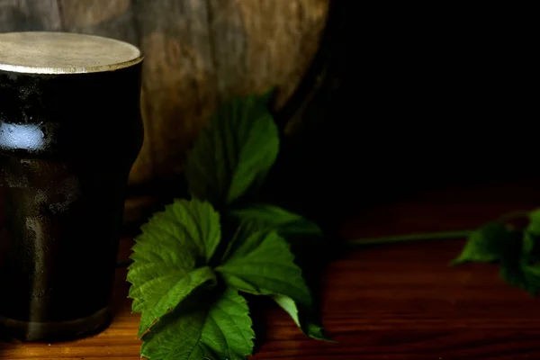 Pinte de bière brune bien avec une feuille de houblon sur le fond du baril. Gros plan . — Photo