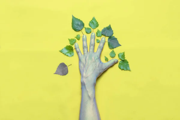 Concepto verde. Mano con hojas en forma de árbol sobre fondo amarillo. Una hoja se marchitó y cayó de un árbol — Foto de Stock