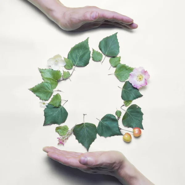 Recycle concept. Hands. Place for an inscription, laid out of green leaves and flowers. The background is white. Circle of green leaves and flowers.